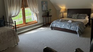 A bedroom with a large bed, a window with curtains, a bedside table with a lamp, and a painting on the wall.