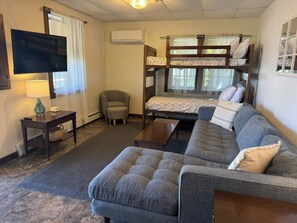 A furnished room with a sofa, a small armchair, a television, an air conditioning unit, and a bunk bed. - Sunnyside Apartment 1#, 1 of 3 - Great location, pool, 1/2 mile to Dreams Park (Cooperstown)