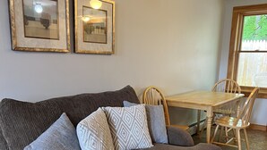 Un soggiorno con un divano grigio, cuscini decorati, un tavolo da pranzo in legno e due quadri appesi al muro.