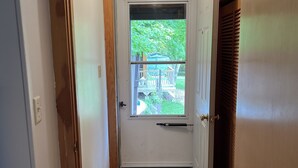Un corridoio stretto con una porta bianca in fondo, una finestra vista verde, e una porta in legno sulla destra.