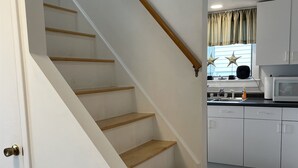 Een wenteltrap met houten treden en een witte muur, leidend naar een keuken met witte kastjes en een magnetron.