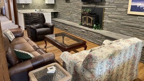 A living room with a leather sofa, a floral armchair, a glass coffee table, and a fireplace. - Sunset Waters -Goodyear Lake - hot tub, swimming ,fishing. paddle sports (Maryland)