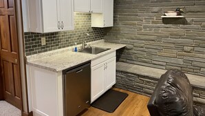A compact kitchen with white cabinets, a granite countertop, a built-in dishwasher, a stone backsplash, and a stone wall. - Sunset Waters -Goodyear Lake - hot tub, swimming ,fishing. paddle sports (Maryland)