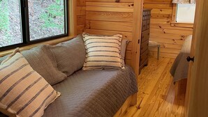 Ein gemütliches Holzhütten-Zimmer mit einem Bett, einem Fenster und einer Tür, die in einen anderen Raum führt.