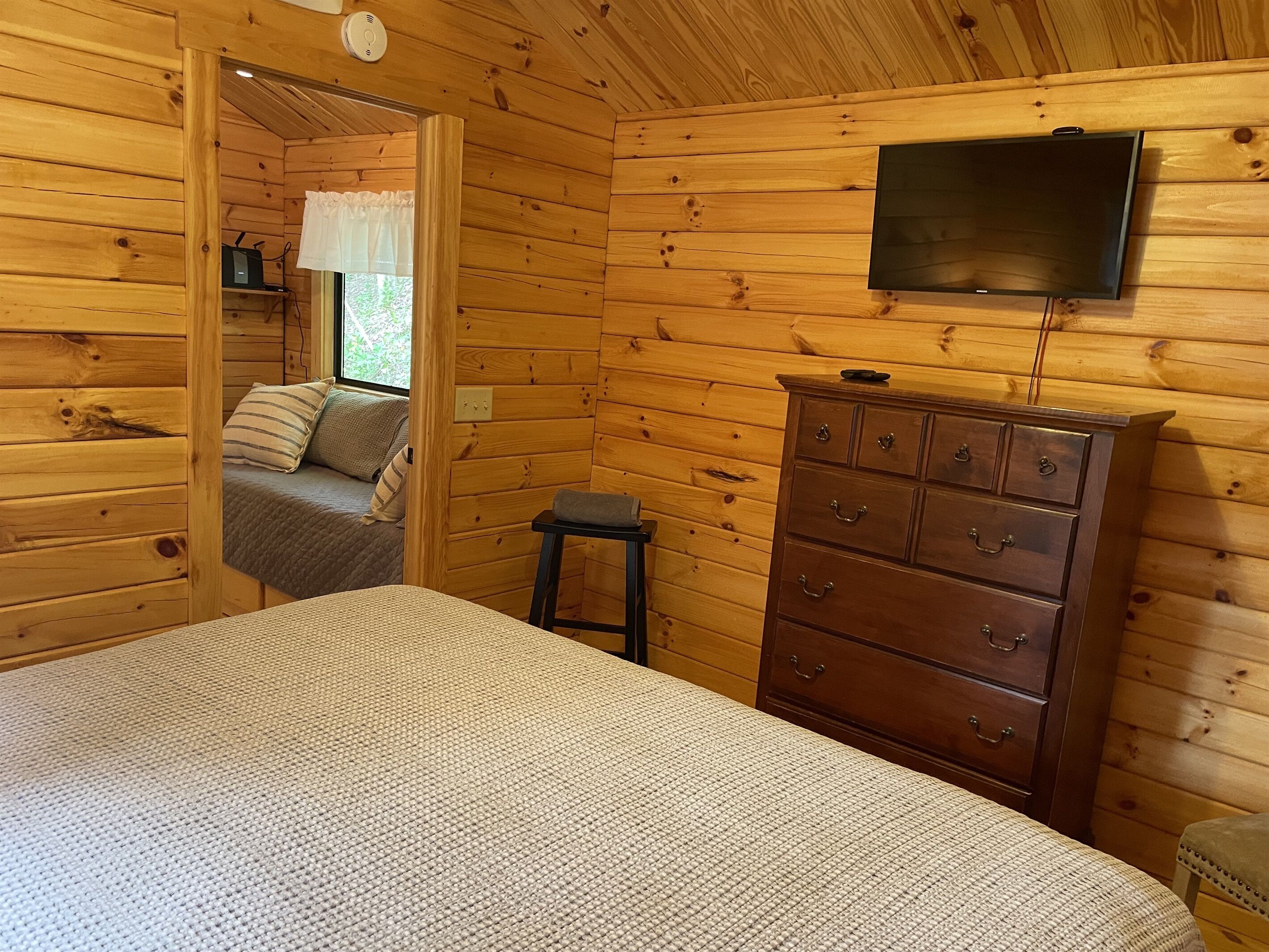 A wooden cabin room with a bed, a dresser, and a television mounted on the wall.