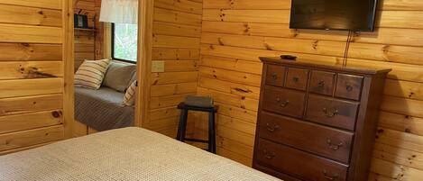 A wooden cabin room with a bed, a dresser, and a television mounted on the wall.