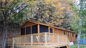Eine Holzhütte mit einer Terrasse, umgeben von Bäumen und einer Rasenfläche.