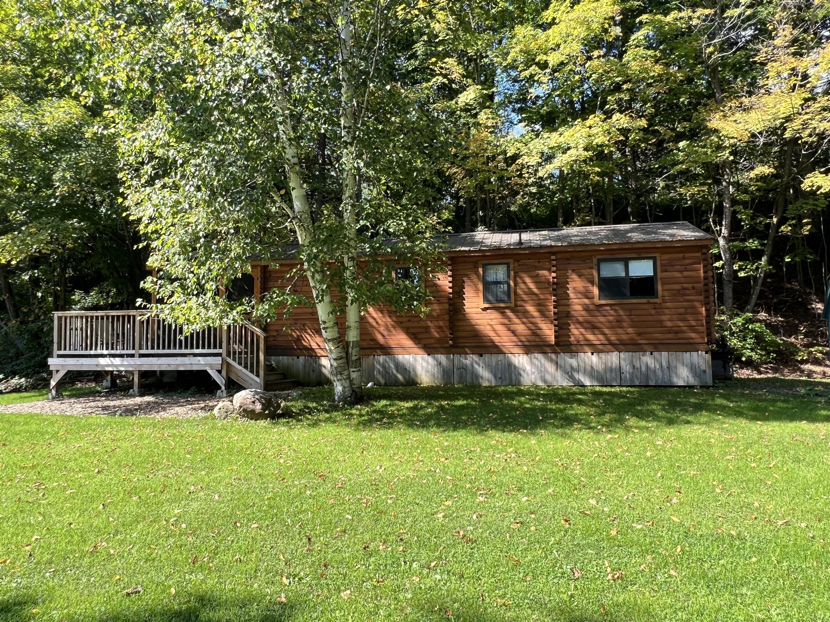 Une cabane en bois dotée d’une terrasse, entourée d’une cour verdoyante et d’arbres.