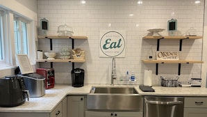 A modern kitchen with white subway tiles, stainless steel appliances, and wooden shelves displaying food items.