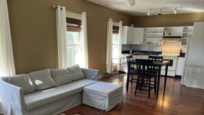 A modern living room with a grey sectional sofa, a round ottoman, and a dining area with a table and chairs.