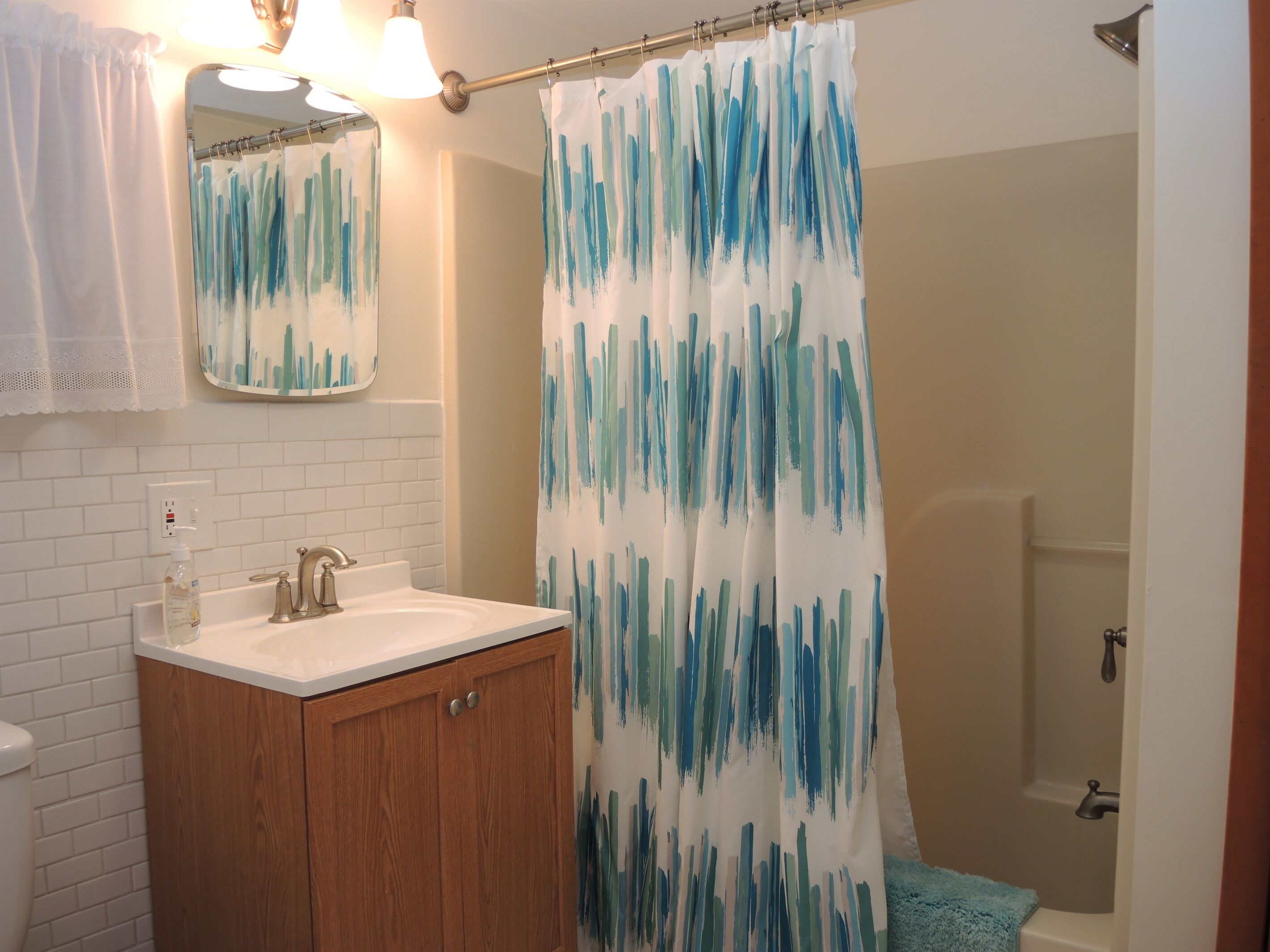 Un baño con un lavamanos blanco, un mueble de madera y una cortina de ducha con un diseño abstracto azul.