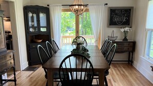 A dining area with a wooden table and chairs, a chandelier, a view of greenery outside, and a chalkboard with a positive message. - Wake Robin Cottage - Recent renovation 4 bdrm/ 4 bath home close to tournaments (Oneonta)
