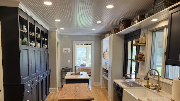 A modern kitchen with dark cabinetry, a wooden bench, a central island, and a window providing natural light. - Wake Robin Cottage - Recent renovation 4 bdrm/ 4 bath home close to tournaments (Oneonta)