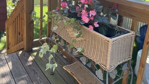 A wooden deck with a wicker planter holding pink flowers and green foliage. - Wake Robin Cottage - Recent renovation 4 bdrm/ 4 bath home close to tournaments (Oneonta)