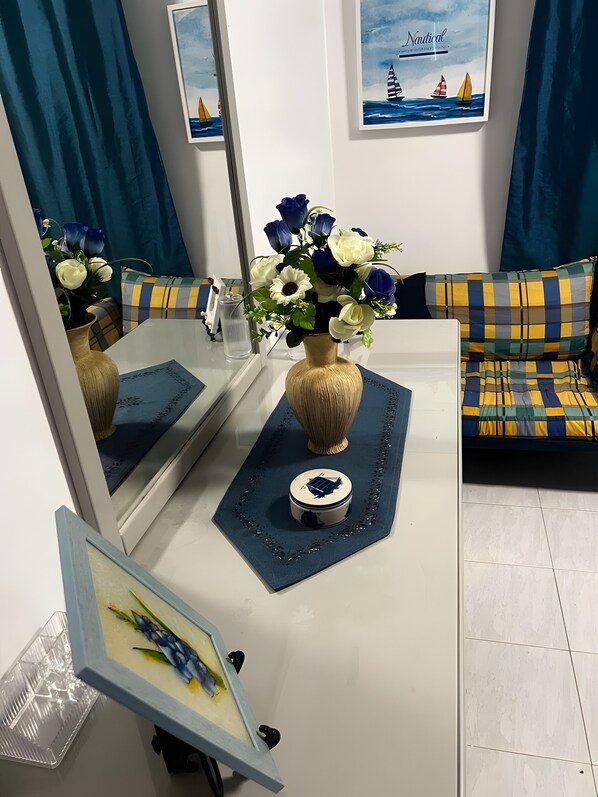 Una sala de estar con un sofá, una mesa de centro con un jarrón de flores, un cuadro enmarcado y un espejo montado en la pared.