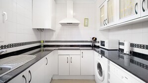 Une cuisine avec des meubles blancs, un plan de travail noir, un lave-linge et un four à micro-ondes.