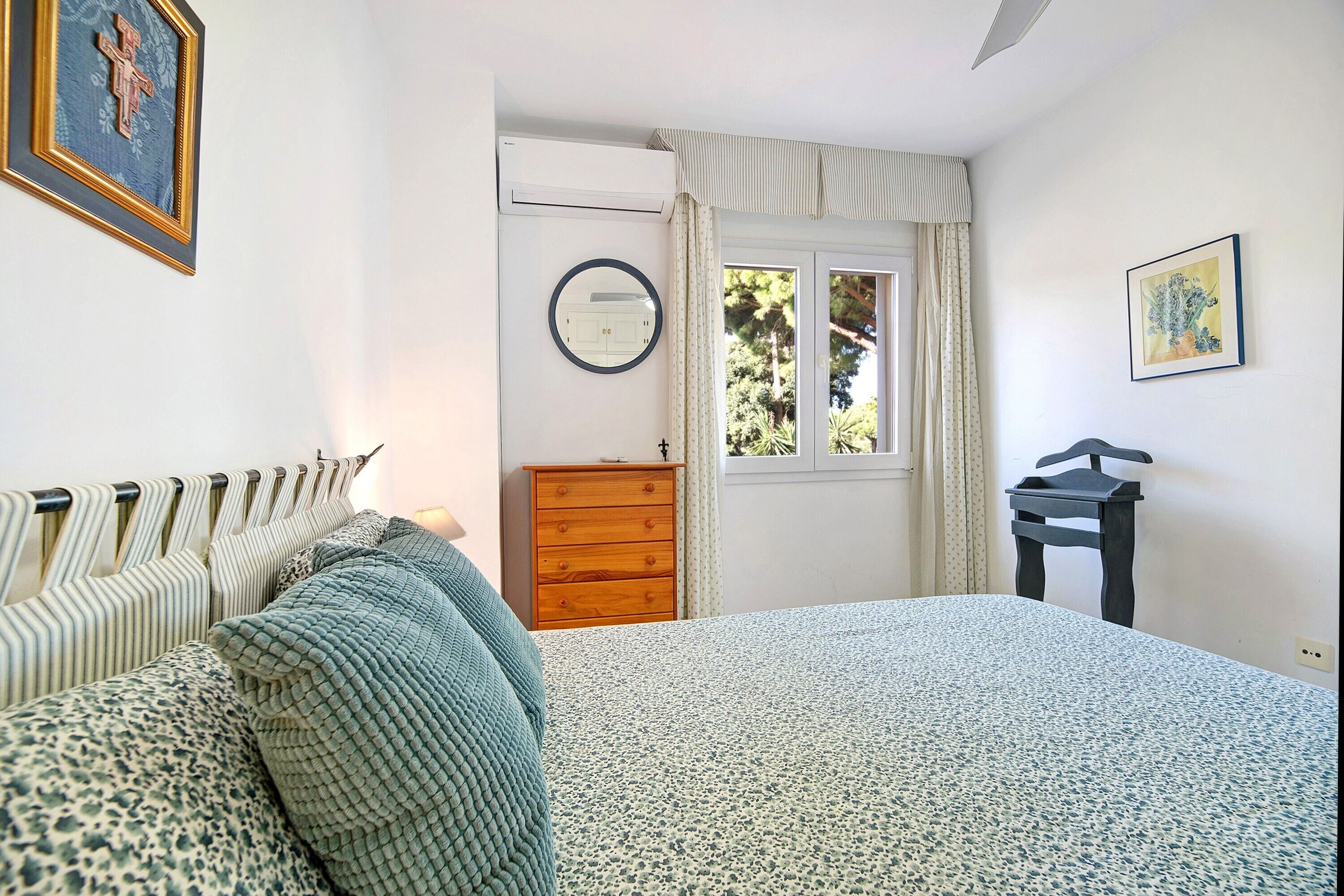 Ein Schlafzimmer mit einem Bett, einem Schminktisch, einem Spiegel und einem Fenster mit Vorhängen.