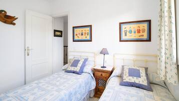 Quarto com duas camas, uma mesa de cabeceira de madeira, uma luminária e duas fotografias emolduradas na parede.