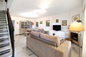 Un salon avec un canapé, un téléviseur, une cheminée et un escalier.