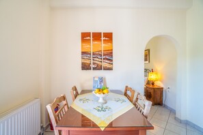 A dining area with a table set for four, a fruit bowl, and a wall-mounted painting.