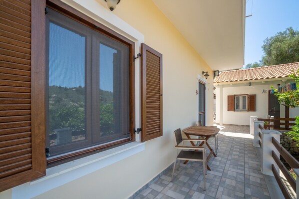 A balcony with a table and chairs, a window with shutters, and a tiled floor.