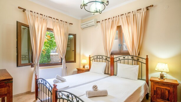Une chambre à coucher comprenant un lit, des rideaux, une table de chevet, une lampe, un appareil de climatisation et une fenêtre donnant sur un paysage verdoyant.