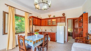 Une cuisine avec des meubles de rangement en bois, une table à manger avec des chaises, un réfrigérateur et un lustre.