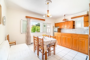 Une cuisine avec des meubles de rangement en bois, une table à manger avec des chaises et une fenêtre avec des rideaux.