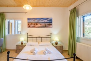 A bedroom with a bed, two bedside tables with lamps, a painting on the wall, and a window with curtains.