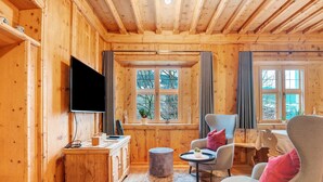 Interior de una cabaña de madera con televisión, asientos y una ventana con vistas.
