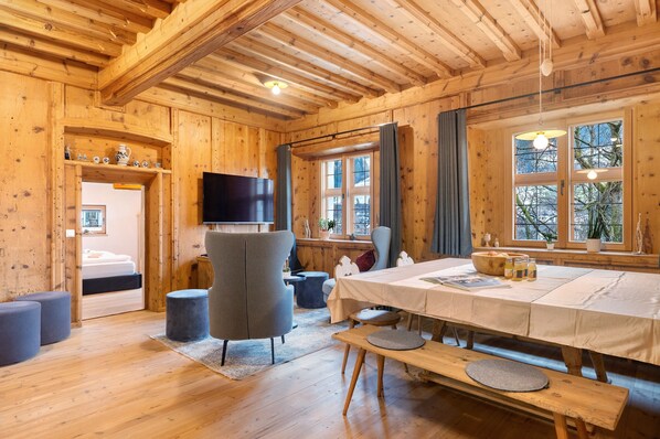 L’intérieur d’un chalet en bois comprend une table à manger, des chaises, un banc, un téléviseur et de grandes fenêtres.