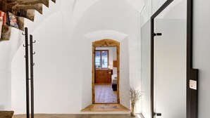 Un pasillo con una puerta de madera que da a una habitación, un perchero y una planta pequeña.
