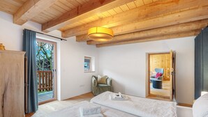 Una habitación con dos camas, techo de madera, puerta corrediza a un balcón y una silla pequeña.