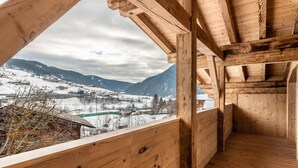 A wooden interior with a view of snow-covered mountains and a village. - Apartment 'Alpin Chalet Samer Fürstenblick' with Mountain View, Terrace and Wi-Fi (Sarntal)