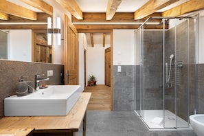 A modern bathroom with a large sink, a glass shower enclosure, and wooden beams on the ceiling.