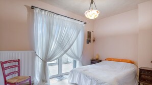 Een slaapkamer met een bed, een stoel, een nachtkastje en een raam met gordijnen.