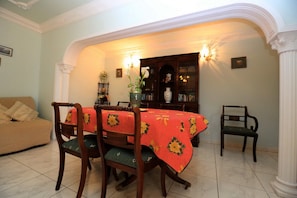 A dining room with a table set for four, surrounded by chairs, a sofa, and a bookshelf.