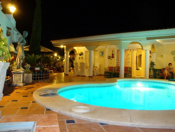 A swimming pool with a tiled deck, a covered patio area with seating, and a statue. - Luxury Villa "Violeta" with Sea Views, Private Pool, Terraces, and Wi-Fi (Adeje)