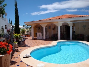 A swimming pool with a tiled deck, a covered patio area, and a statue.