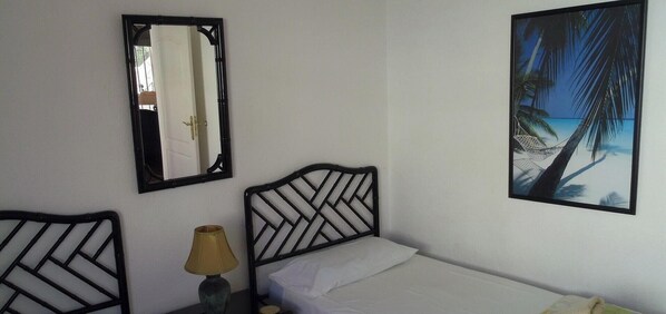 A bedroom with a bed, a nightstand, a lamp, a mirror, and a framed picture of a beach scene.