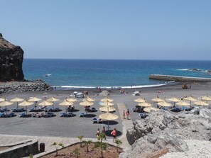A beach with umbrellas, lounge chairs, and a rocky cliff.