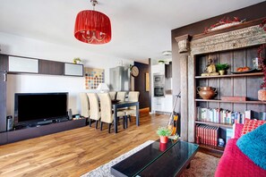 Un salon moderne doté d’un téléviseur à écran plat, d’un coin repas, de bibliothèques et d’un luminaire suspendu rouge.
