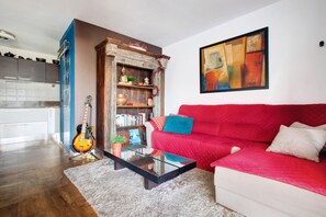 Un salon avec un canapé rouge, une table basse en verre, une bibliothèque et une guitare.