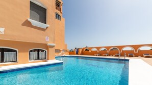 Una piscina amb aigua cristal·lina blava, envoltada per un edifici amb parets taronja i finestres d'arc.