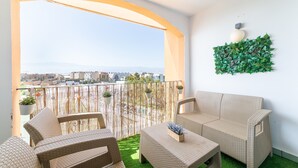 Un balcó amb mobiliari de vimet, gespa artificial verda i una paret decorativa amb plantes.