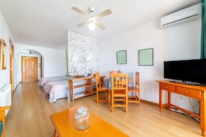 A room with a ceiling fan, a TV, a wooden table, a bed with pink bedding, and a patterned wall.