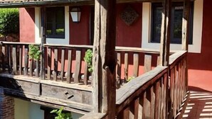Un balcone in legno con ringhiera, affacciato su un edificio rosso con finestre e tetto in tegole.