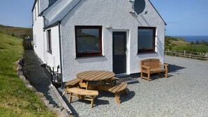 Ein weißes Haus mit Kiesterrasse, Holzmöbeln und Meerblick.