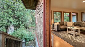A wooden deck with a view of a forest. Inside, there is a sofa and a coffee table. - Eagle's Nest Suite-Inlet, Forest Views, Marina (Tofino)