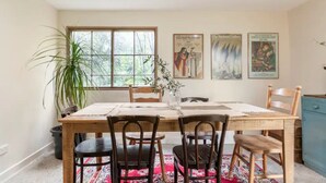 Un comedor con una mesa de madera, cuatro sillas, un jarrón con flores y una ventana que da a vistas de follaje.